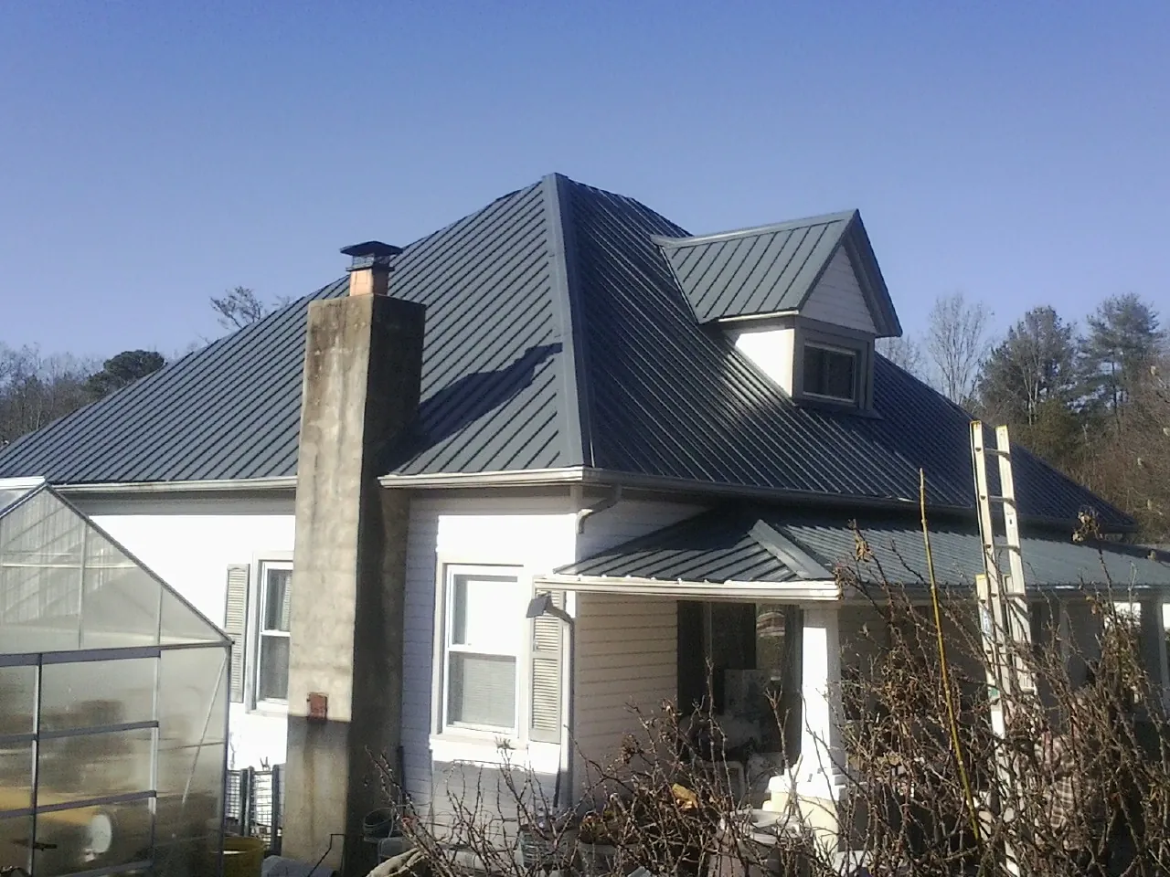 Dark blue standing seam metal roof on a white farmhouse with dormer — Slate & Tile Roof Repair by Roofing Brothers in Simpsonville
