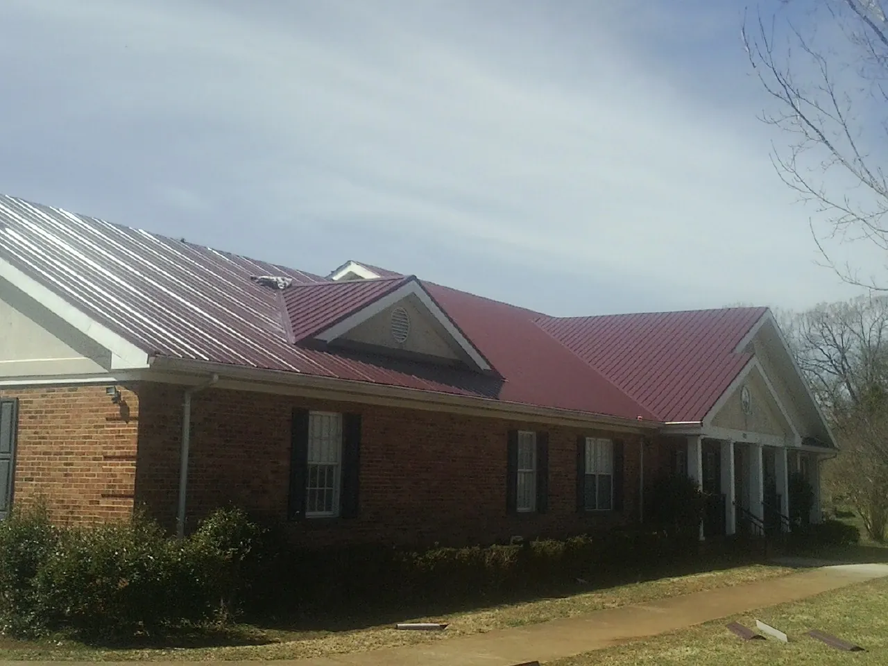 Red metal roof with gabled entries on a long brick building, from a Hail Damage Roof Repair job in Simpsonville