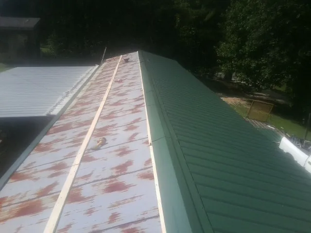 Old rusted panels beside newly installed green metal roofing — Wind Damage Roof Repair by Roofing Brothers in Simpsonville