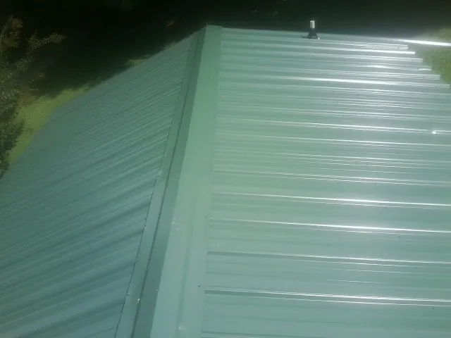 New green metal panels meeting at the ridge of a roof — Flat Roof Repair work by our crew in Simpsonville